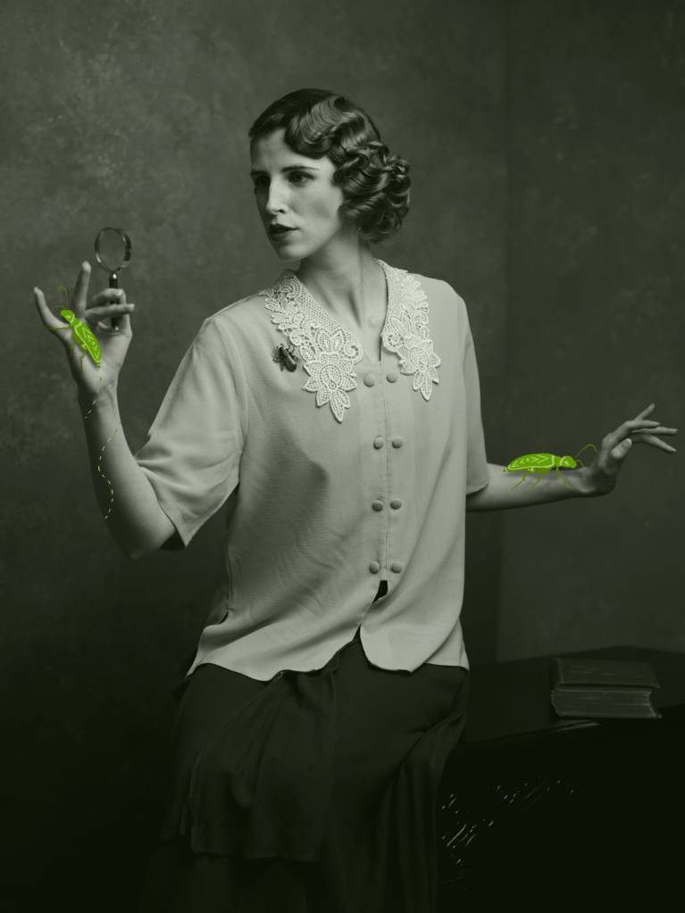 Laura Crow in Earwig, wearing a 1920s blouse with a large lace collar and with finger-waved vintage hair. She is holding a magnifying glass and examining an illustrated green beetle.