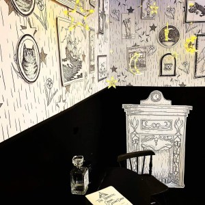 The set of short film, Queen of Swords. There are two walls covered in framed pictures, a fireplace, a clock, and a table. Everything is styled to look like hand-drawn black and white illustrations.